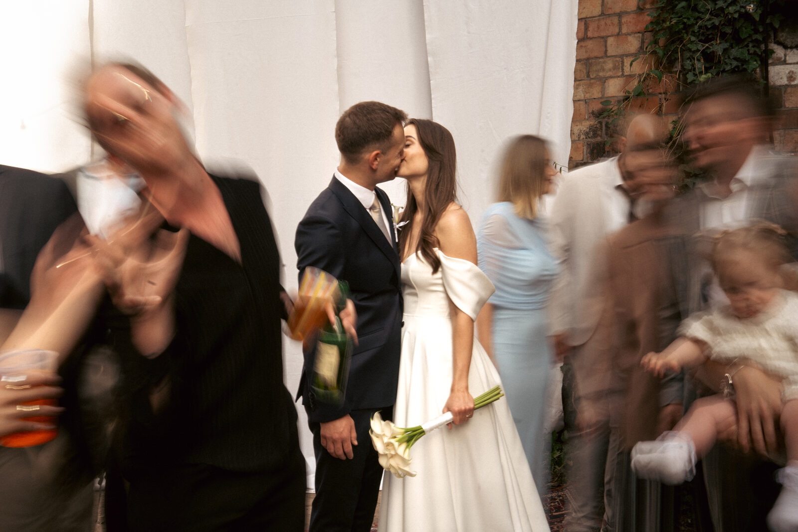 Bride and groom kissing surrounded by moving guests