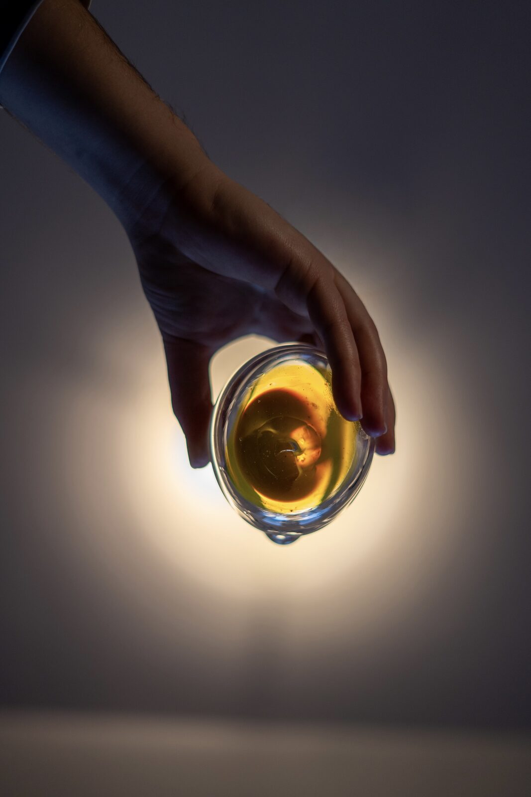 A hand holding a backlit glass with amber liquid