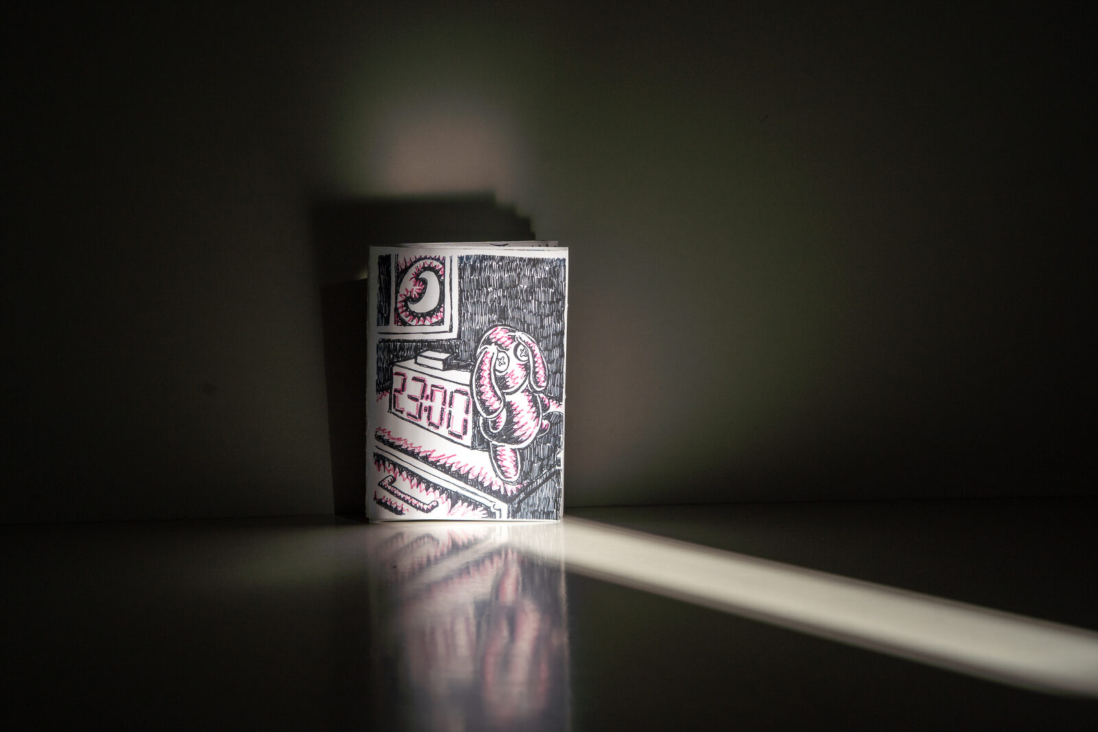 A hand-drawn zine standing upright in a shaft of light