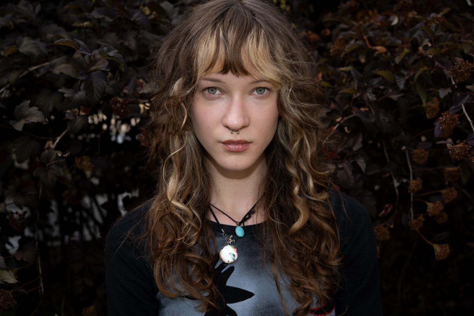 Close portrait of a woman with curly hair against dark foliage