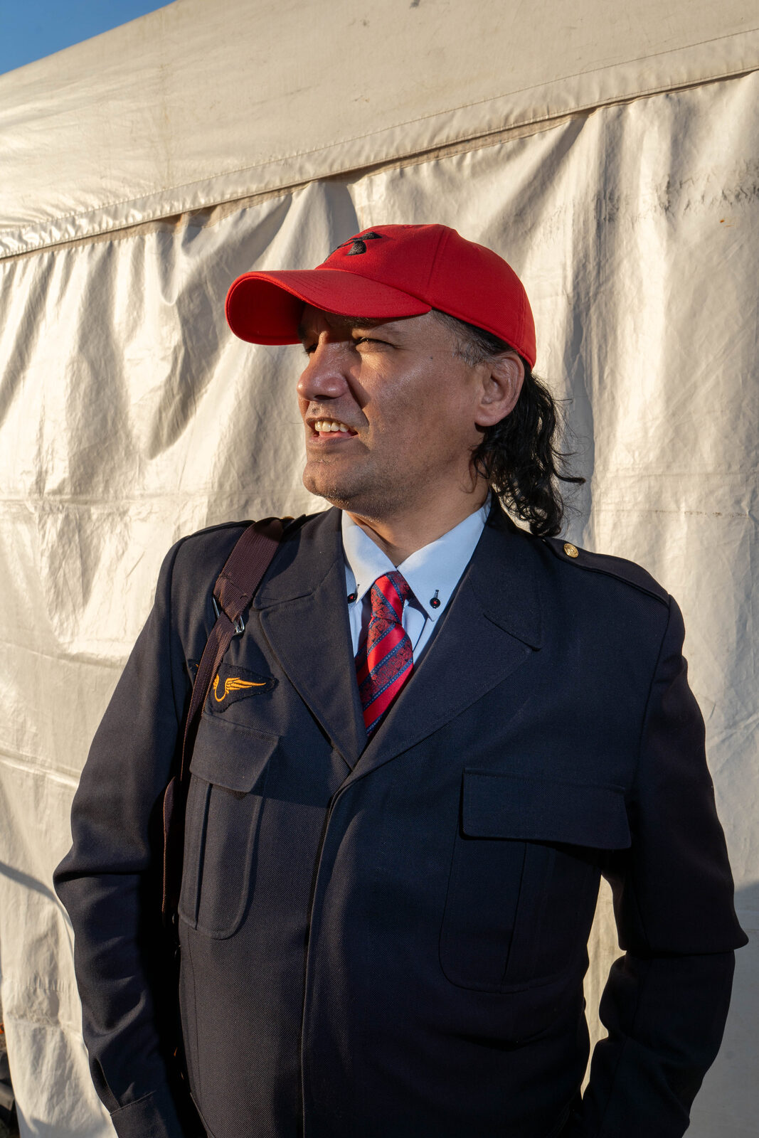 Man in a red cap and dark uniform lit by low sun