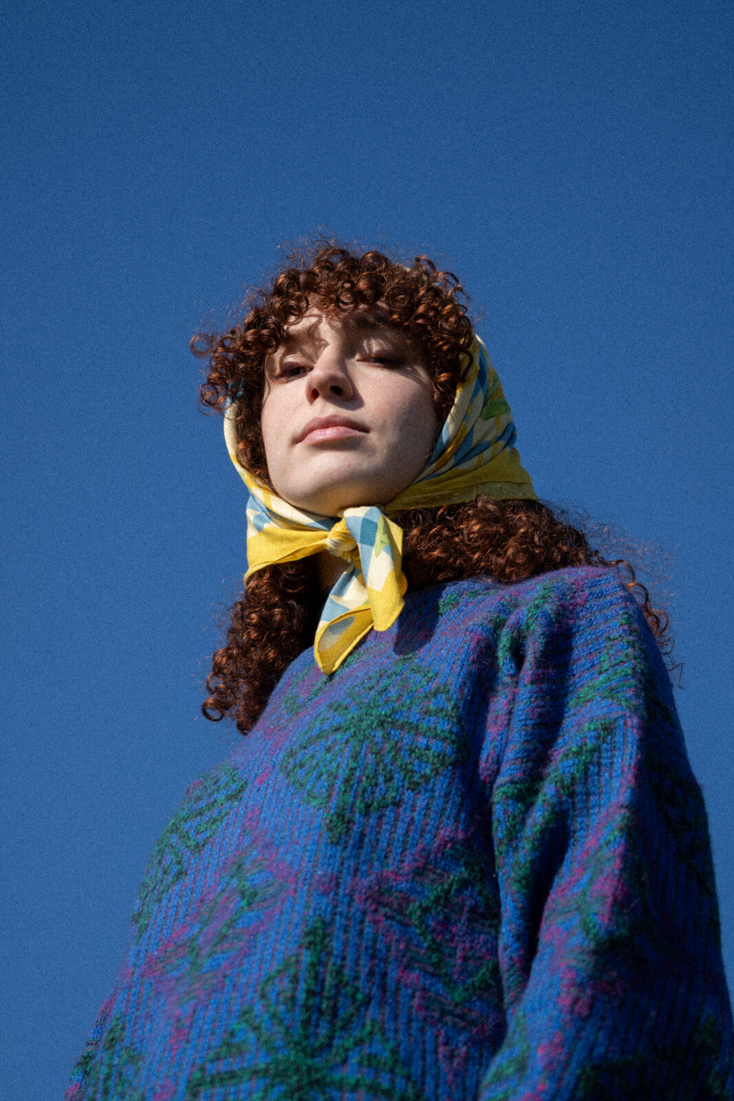 Woman in a yellow headscarf looking up against a deep blue sky